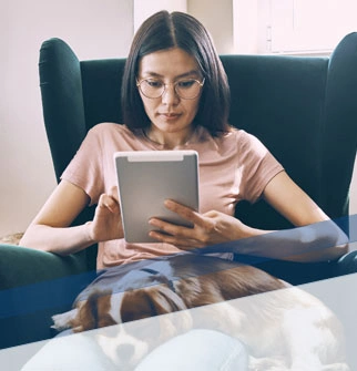 woman sitting down in a chair using a tablet with a dog on her lap